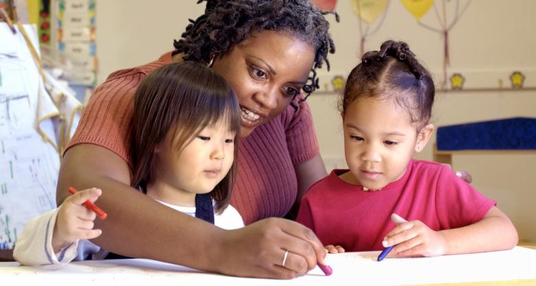 A school teacher drawing with two young students.