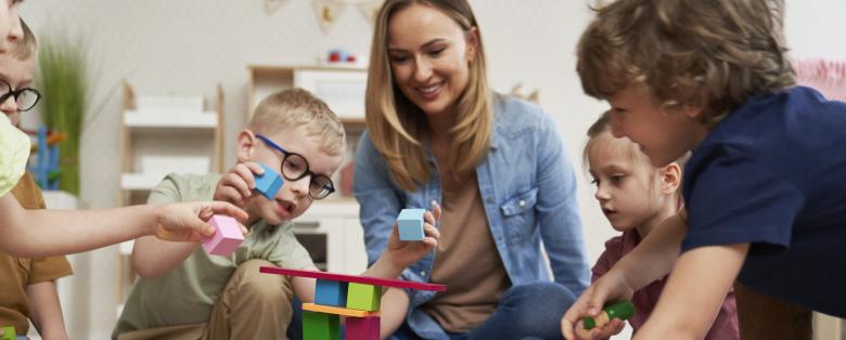 A woman playing with young children and blocks.